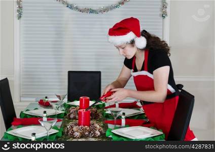Young teenage girl, dressed in Santa outfit, lighting candle for holiday party at the dining room table