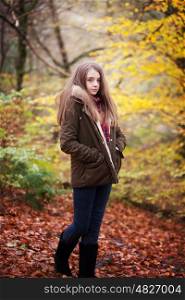 Young teenage girl standing with her hands in her coat pockets in a forrest in Autumn