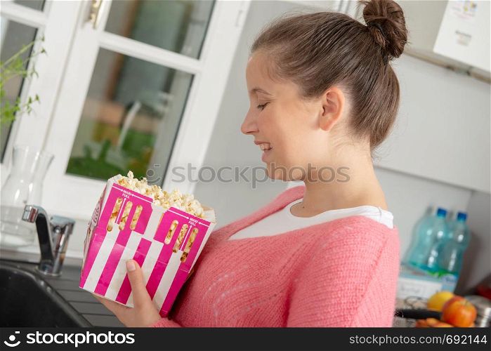 young teenage girl with a pink sweater eating popcorn at home