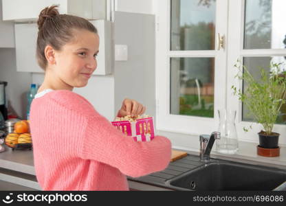 young teenage girl with a pink sweater eating popcorn at home