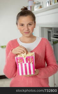 young teenage girl with a pink sweater eating popcorn at home