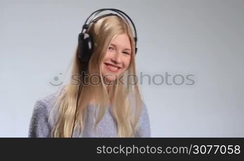 Young teenage woman listening to music intensely in her headphones over white background. Attractive girl hearing the music fading, touching the earcup and slowly taking headphones off, hanging them around her neck and smiling into the camera.