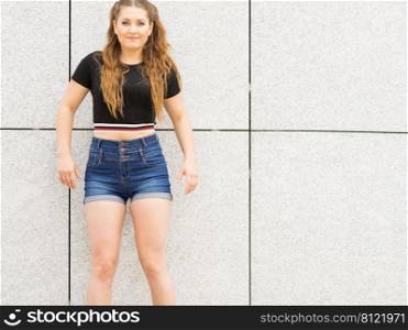 Young teenage woman wearing denim shorts and black crop top. Female presenting fashionable summer outfit.. Fashionable teen presenting summer outfit