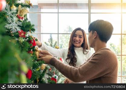 Young Teenager asian couple decorating Christmas tree together prepare for Christmas party holiday.