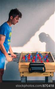 Young teenager boy playing table football with another player. Young people having fun, spending time together