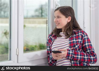 young teenager girl using phone near the window