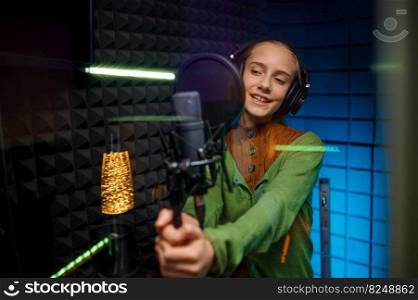 Young teenager singer artist wearing headphones singing recording new song with microphone at record studio. Young teenager singer artist singing