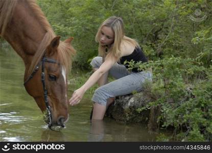 young teenager with her brown stallion in a river (focus on the woman)