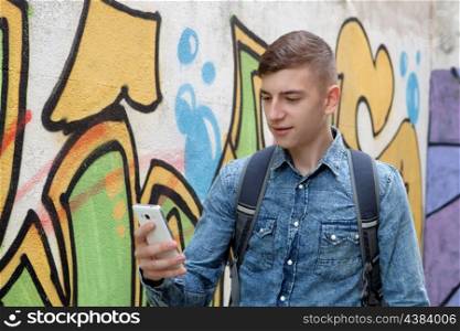 Young teenager with her cell phone and near of a wall painted with graffiti
