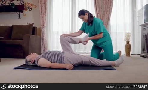 Young therapist exercising with older female patient in nursing home. Nurse giving leg massage to senior woman in a retirement home. Hand held movement