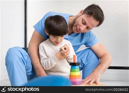 Young therapist helping cute little boy who has cerebral palsy, playing with developing toy at rehabilitation clinic. High quality photo. Young therapist helping cute little boy who has cerebral palsy, playing with developing toy at rehabilitation clinic.