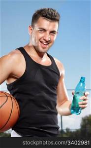 Young thirsty man drinking water on sports field