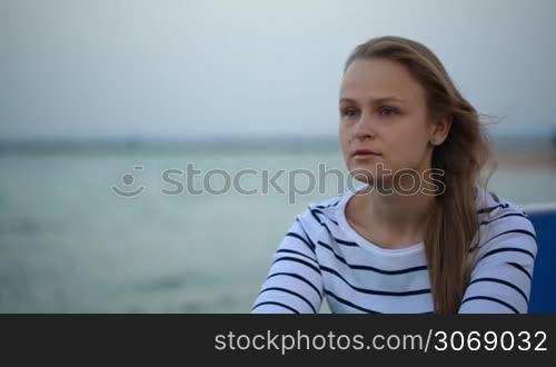 Young thoughtful woman sitting by the sea and looking into the distance