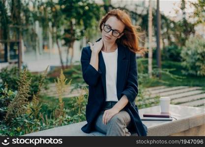 Young tired businesswoman massaging neck, feeling pain in body muscles because of bad posture at work, sitting in park after long working day in office, overworked female suffering from backache,. Young tired woman massaging neck, feeling pain in body muscles because of bad posture at work