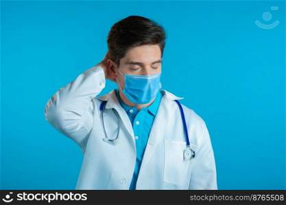 Young tired doctor man in professional medical white coat having headache, studio portrait. Guy putting hands on head, isolated on blue background. Concept of problems, medicine, illness.. Young tired doctor man in professional medical white coat having headache, studio portrait. Guy putting hands on head, isolated on blue background. Concept of problems, medicine, illness