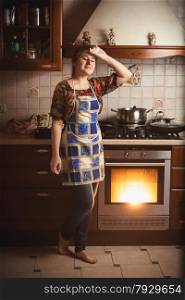 Young tired housewife standing near working oven