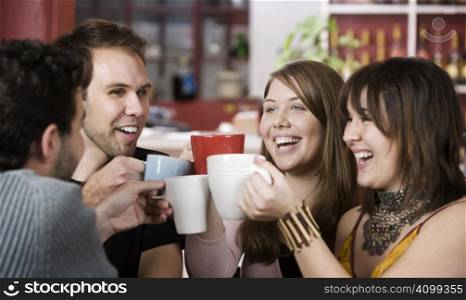 Young toasting friends with coffee cups in a cafe