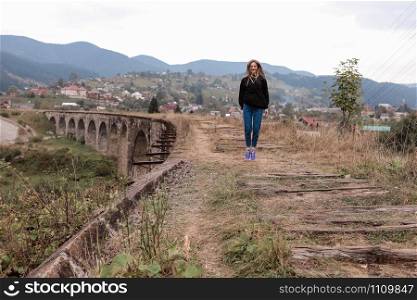 Young tourist girl walks the old railway tracks on the viaduct. Old railway viaduct in the mountain resort village of Vorokhta. Ukraine, Carpathians.