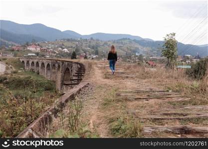 Young tourist girl walks the old railway tracks on the viaduct. Old railway viaduct in the mountain resort village of Vorokhta. Ukraine, Carpathians.