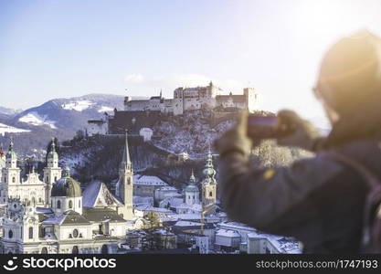 Young tourist man is making a photo of Salzburg with her smartphone, winter time