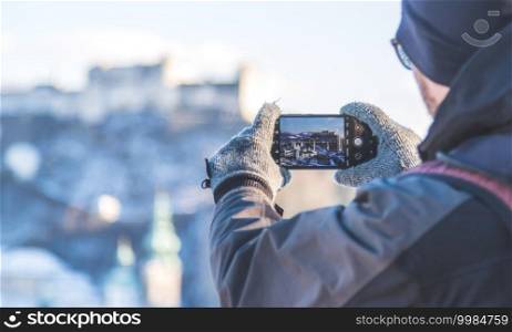 Young tourist man is making a photo of Salzburg with her smartphone, winter time