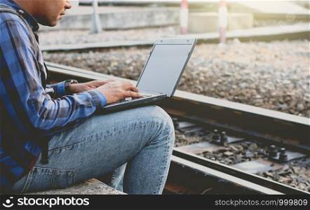 Young tourists are using a notebook computer near the railroad tracks.