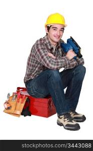 young tradesman sitting on toolbox holding sander machine