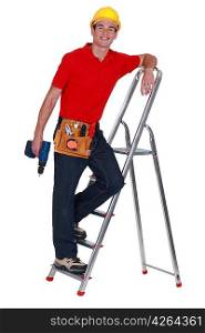 Young tradesman standing on a stepladder and holding a screw gun