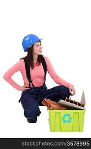 Young tradeswoman squatting beside a recycling bin
