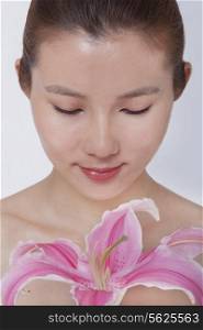 Young tranquil woman looking down at a large pink flower, studio shot