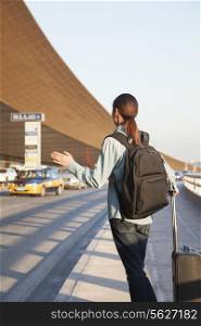 Young traveler hailing a taxi at airport