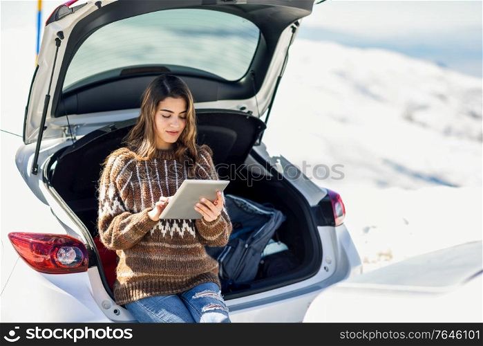 Young traveler woman using digital computer in snowy mountains in winter, in Sierra Nevada, Granada, Spain. Female wearing winter clothes.. Young traveler woman using digital computer in snowy mountains in winter.