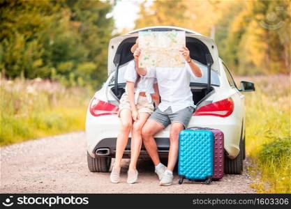 Young travelers looking at map while sitting in trunk of a car. Summer car vacation. Young couple tourist enjoying on summer vacation