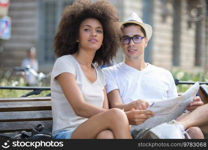 young traveling couple checking the map on a bench