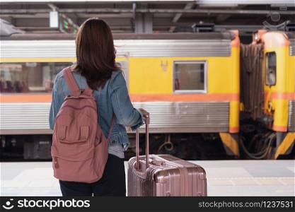 Young traveller girl in jeans jacket with pink bag and luggage waiting for the train on the platform, copy space, travel or transportation concept