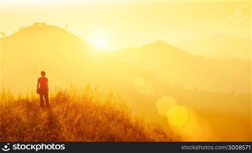 Young traveller standing at mountain at sunrise. Travel, vacation, freedom or success concept.