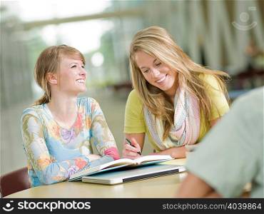 Young tutor writing in student&acute;s book, smiling