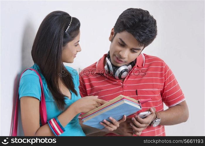 Young university students discussing over book against wall