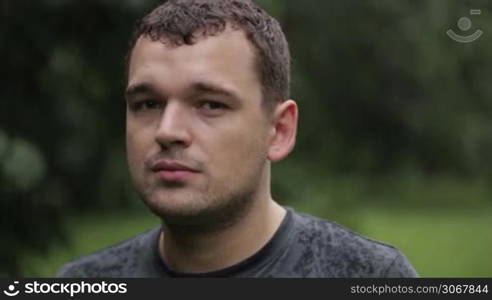 Young unshaven man getting wet under the rain and looking to the camera. Close up portrait.