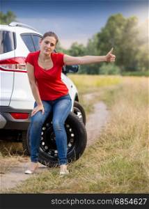 Young upset woman sitting at broken car and hitchhiking