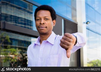Young urban businessman showing thumb down. Outdoors.