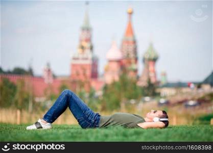 Young urban man relaxing on the grass listening the music outdoors on background of St Basils Church in Moscow. Happy young urban man enjoy his break in the city