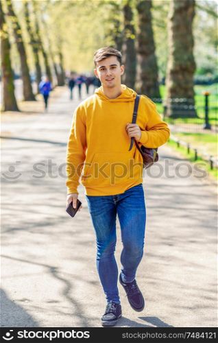 Young urban man using smartphone walking in street in an urban park in London, UK.. Young urban man using smartphone walking in street in an urban park in London.