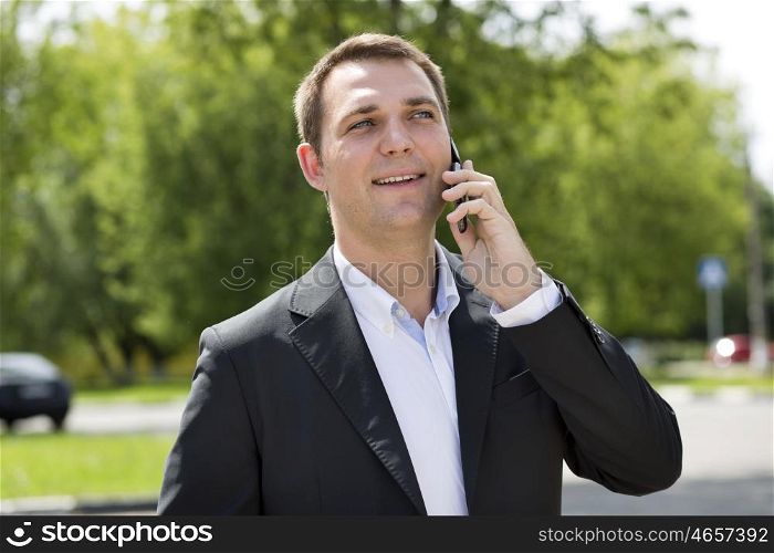 Young urban professional man talking on smartphone. Close up portrait of male business man on smart phone outdoors in suit jacket. Handsome modern guy.