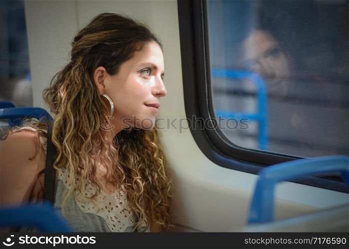 Young urban woman looking through the window in a train. Modern people lifestyle.