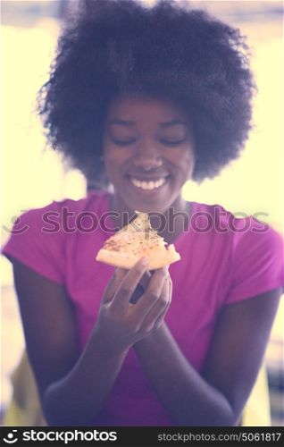young very hangry african american woman with afro hairstyle eating tasty pizza slice in fast food restaurant