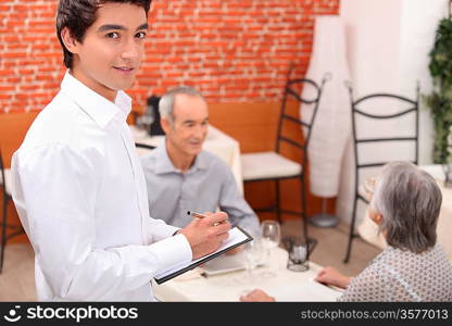 Young waiter approaching an older couple to take their order in a restaurant