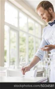 Young waiter arranging wineglasses on table at restaurant