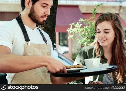 Young waiter holding tray and serving coffee to female customer.