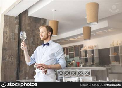 Young waiter looking at empty wineglass in restaurant